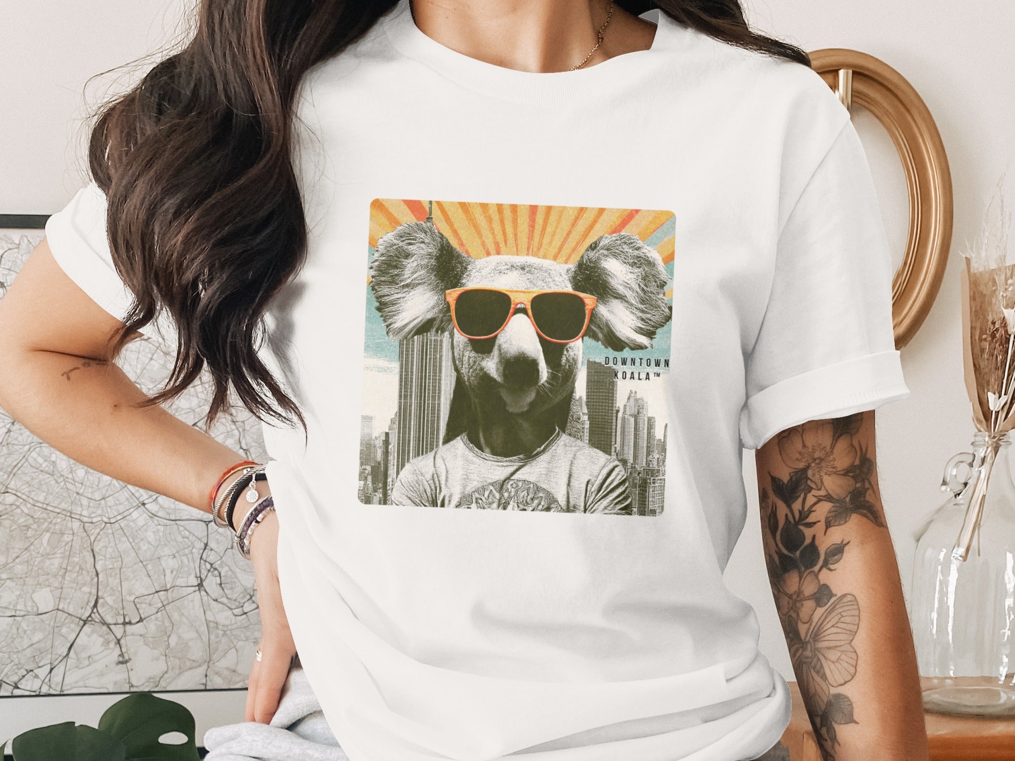 White t-shirt with illustration of a koala wearing sunglasses and a city skyline.
