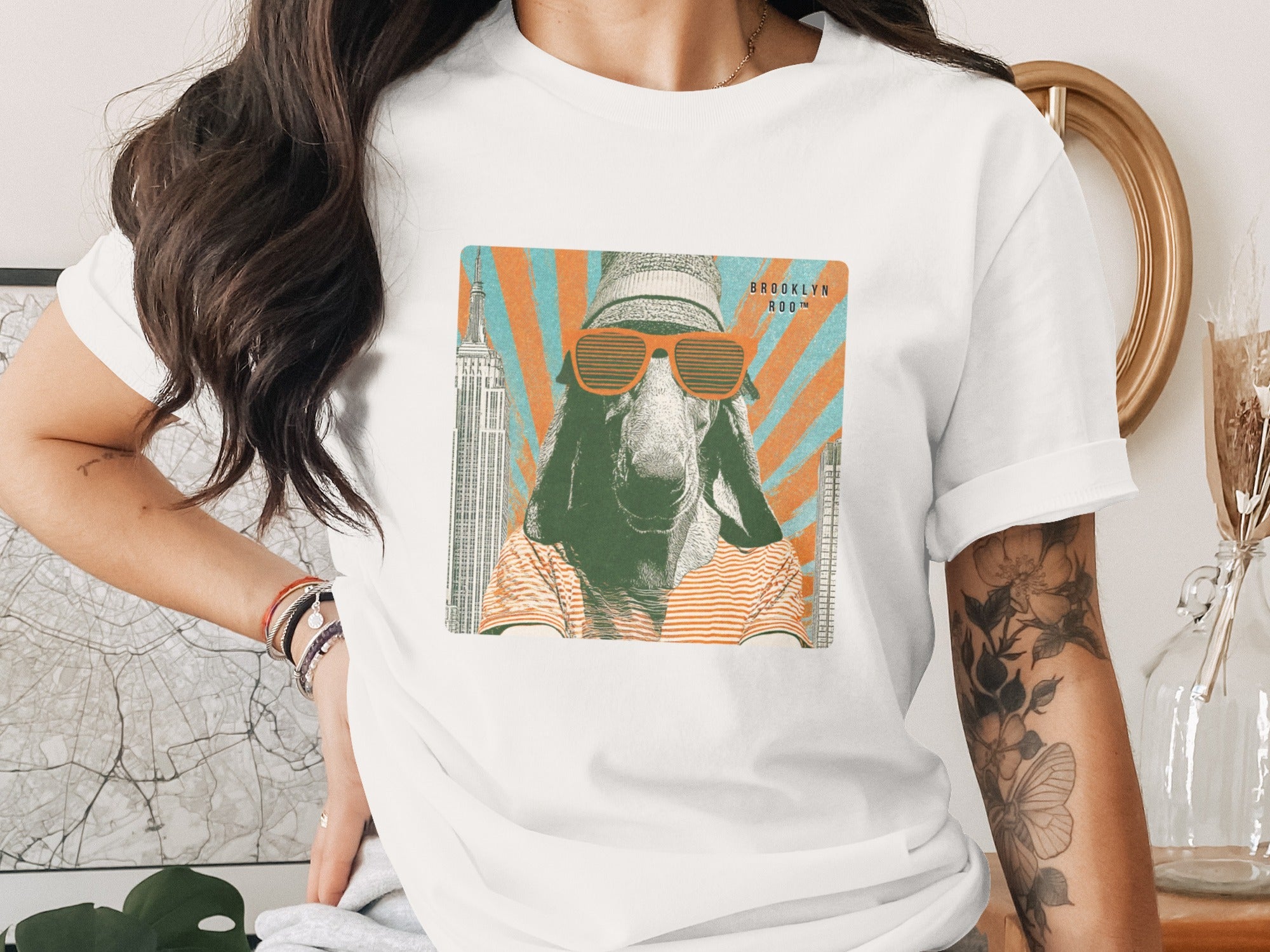T-shirt with graphic of a goat wearing sunglasses, striped shirt, and beanie, with Empire State Building.