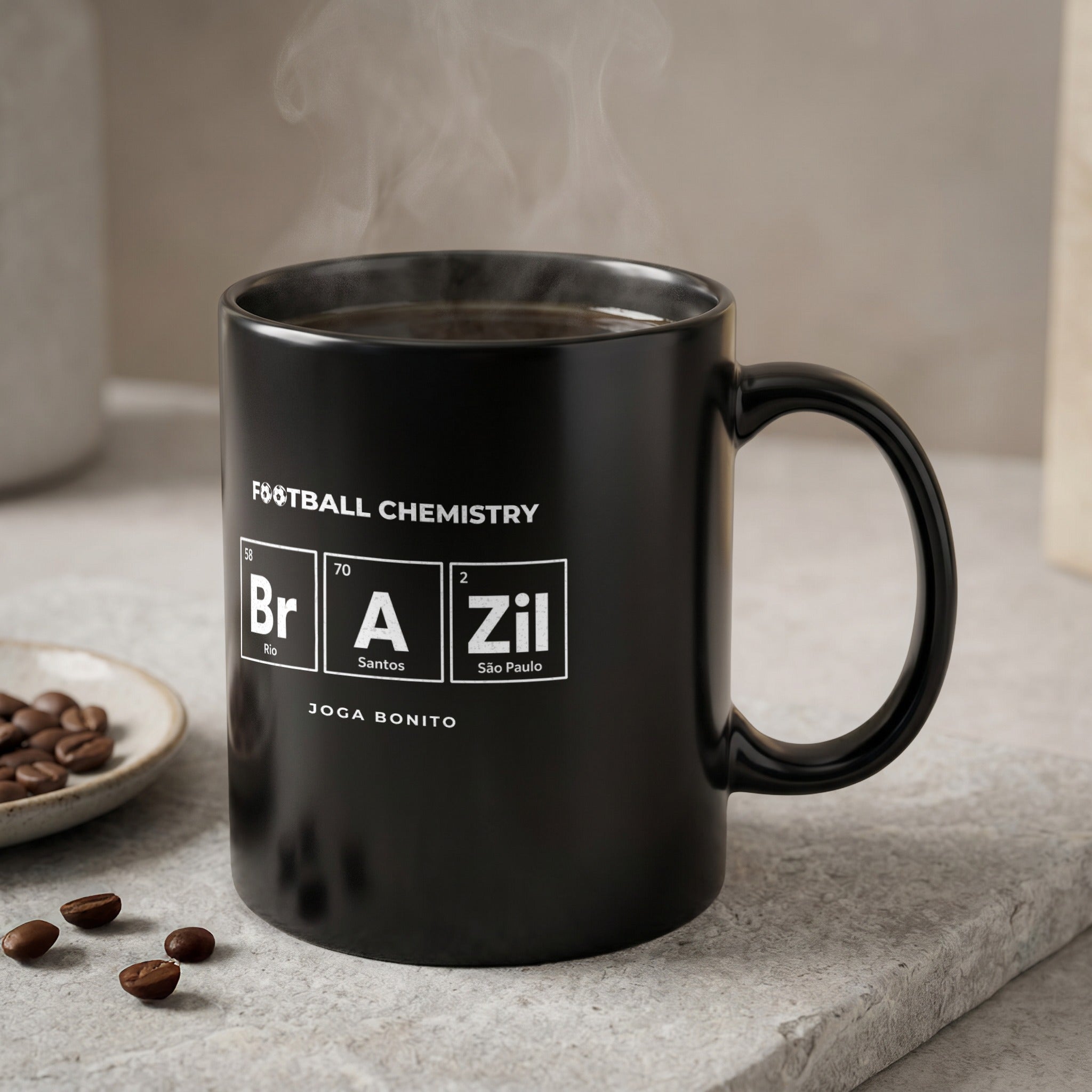 Black mug with "Football Chemistry" and periodic table elements, next to coffee beans.